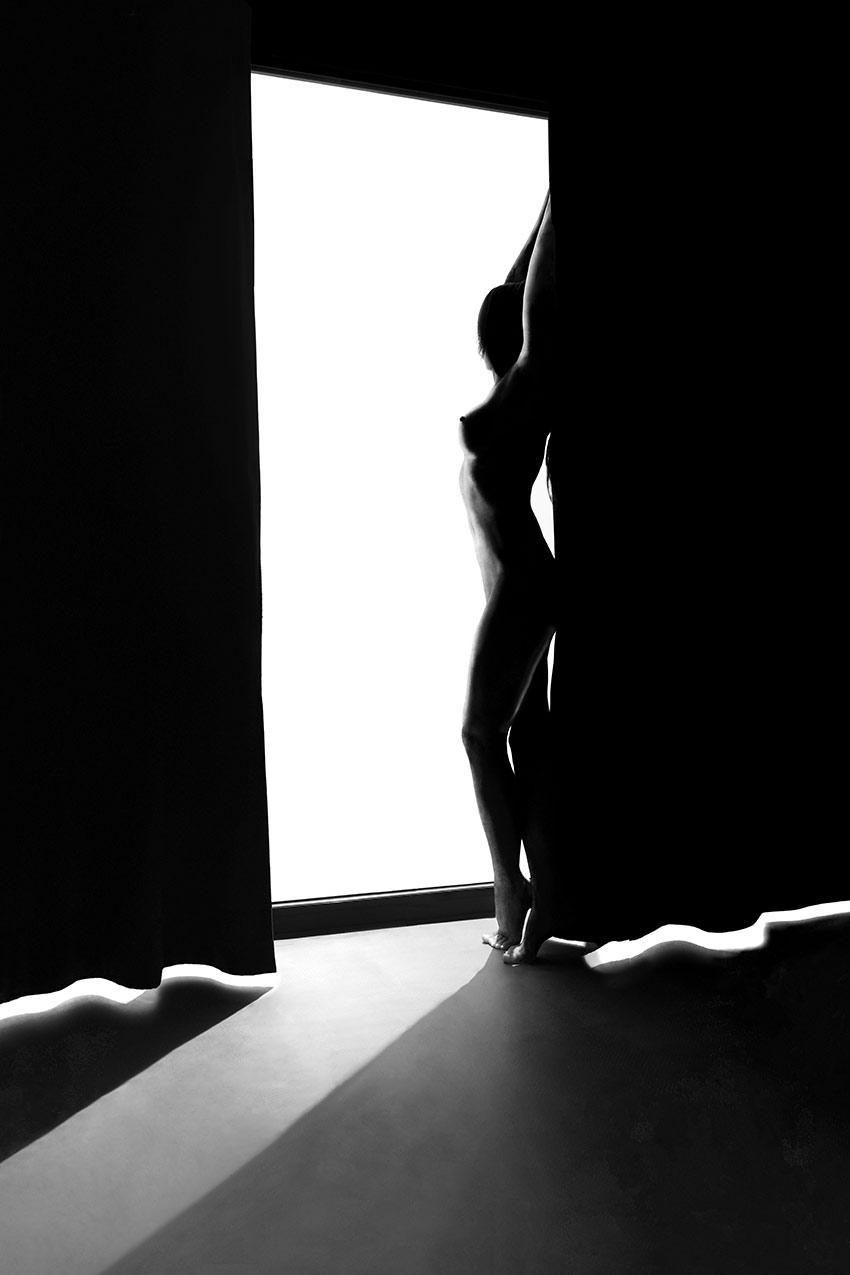 Будуарная фотография в черно-белом цвете. Фотосъемка обнаженной натуры у окна при контровом свете для захватывающей игры теней.